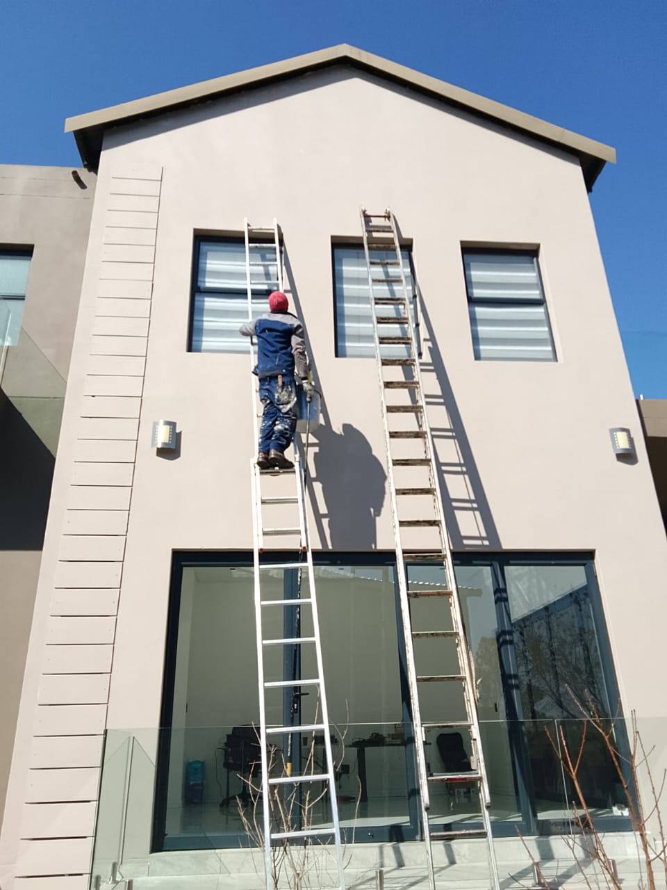 worker on a ladder painting a double storey building